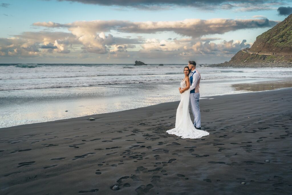 Postboda en Tenerife: Irina y David en Almáciga 18 Postboda en Tenerife: David abrazando a Irina en la arena negra con el acantilado verde al fondo