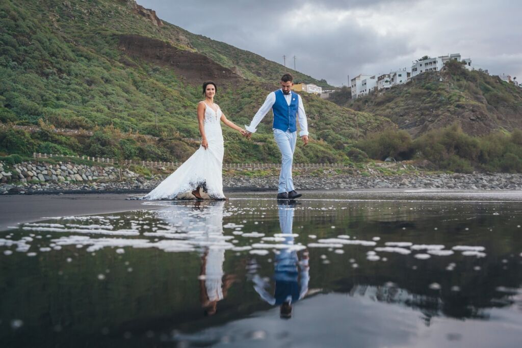 Postboda en Tenerife: Irina y David en Almáciga 10 Postboda en Tenerife: Irina y David caminando de la mano por la arena húmeda con reflejo en Almáciga