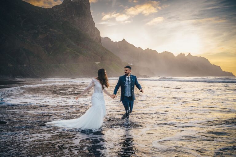 Cómo trabajo: fotógrafo bodas en Tenerife 25 Novios cogidos de la mano caminando entre las olas en una playa de Anaga (Tenerife) al atardecer, durante su sesión de postboda