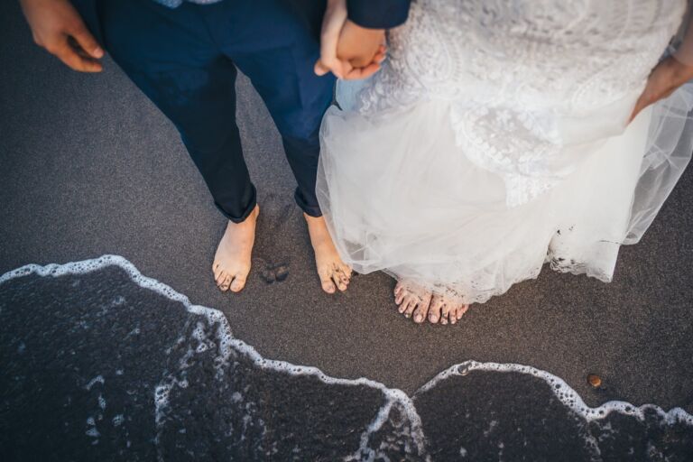 Cómo trabajo: fotógrafo bodas en Tenerife 15 Detalle de los pies descalzos de una pareja de novios cogidos de la mano sobre la arena negra de una playa de Anaga (Tenerife), con la espuma del mar en la orilla, durante su postboda