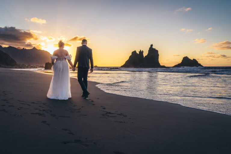Cómo trabajo: fotógrafo bodas en Tenerife 10 Pareja de novios caminando de espaldas, cogidos de la mano, por la playa de Benijo (Anaga, Tenerife) hacia sus roques al atardecer durante su sesión de postboda