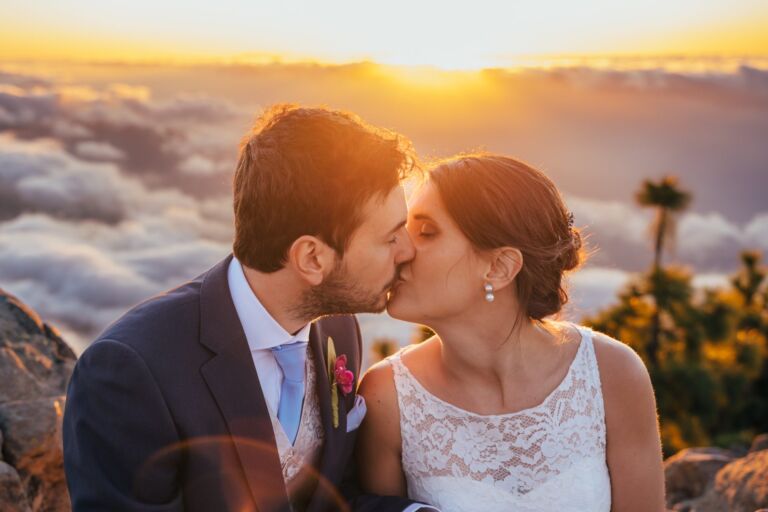 Cómo trabajo: fotógrafo bodas en Tenerife 26 Primer plano de una pareja de novios besándose al atardecer sobre el mar de nubes de Tenerife, durante su sesión de postboda