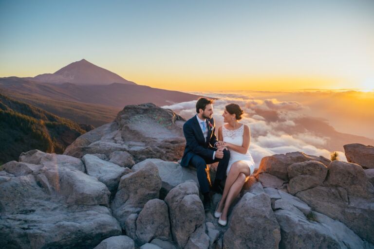 Cómo trabajo: fotógrafo bodas en Tenerife 16 Pareja de novios sentados en unas rocas sobre el mar de nubes al atardecer, con el Teide al fondo, durante su sesión de postboda en Tenerife