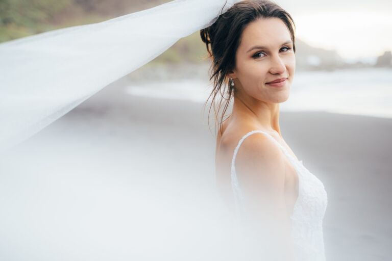 Cómo trabajo: fotógrafo bodas en Tenerife 12 Retrato de una novia sonriendo a cámara con el velo ondeando al viento en una playa de Tenerife durante su sesión de postboda