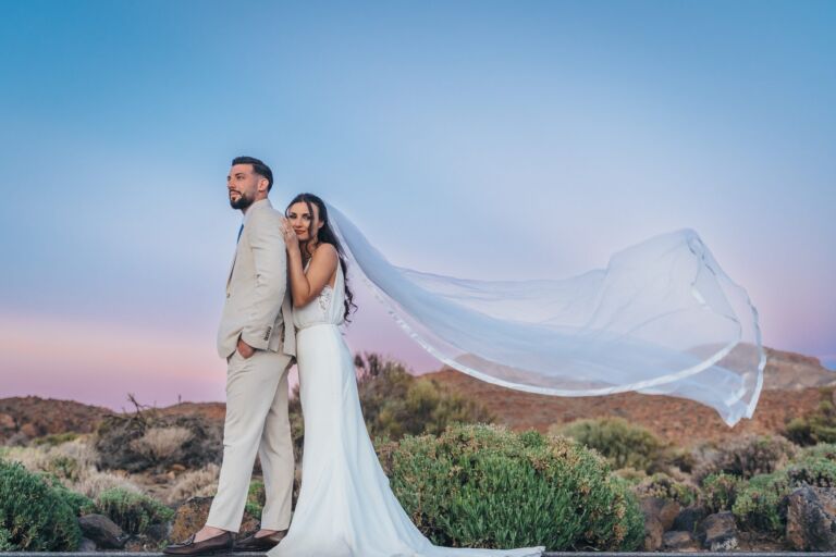 Cómo trabajo: fotógrafo bodas en Tenerife 27 Novios al atardecer en el Parque Nacional del Teide durante su postboda en Tenerife, con el velo de la novia desplegado por el viento sobre el paisaje volcánico