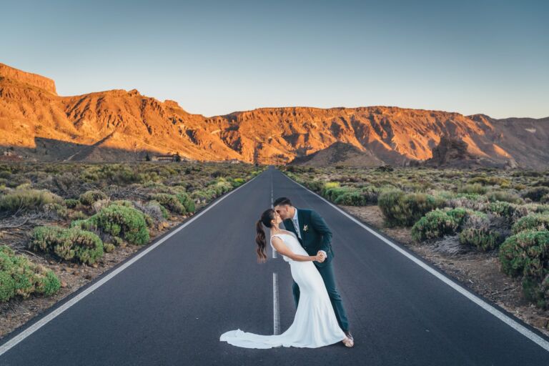 Cómo trabajo: fotógrafo bodas en Tenerife 21 Pareja de novios besándose en mitad de la carretera de las Cañadas, en el Parque Nacional del Teide, durante su postboda en Tenerife, con las paredes volcánicas doradas al fondo