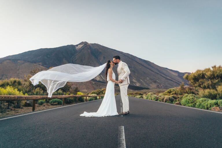 Cómo trabajo: fotógrafo bodas en Tenerife 8 Pareja de novios besándose en una carretera del Parque Nacional del Teide durante su postboda en Tenerife, con el velo de la novia ondeando al viento y el volcán al fondo