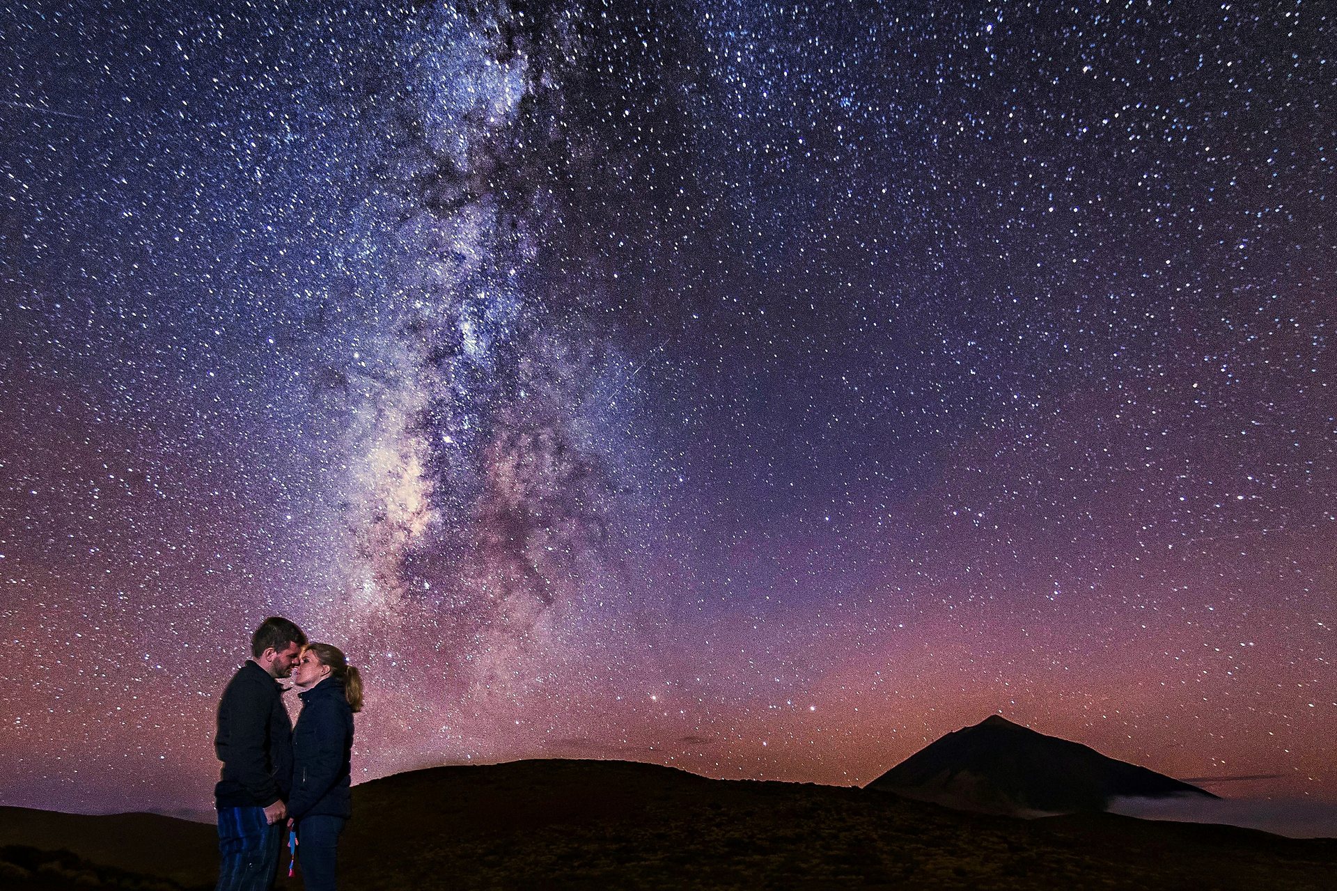 Sesión nocturna en el Teide 8 Una pareja con ropa de abrigo se mira bajo la Vía Láctea, con la silueta del Teide al fondo, durante su sesión de fotos en el Teide